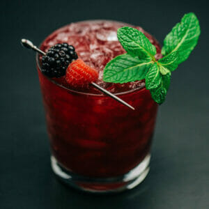 Petite Cup cocktail garnished with fresh berries and a mint sprig